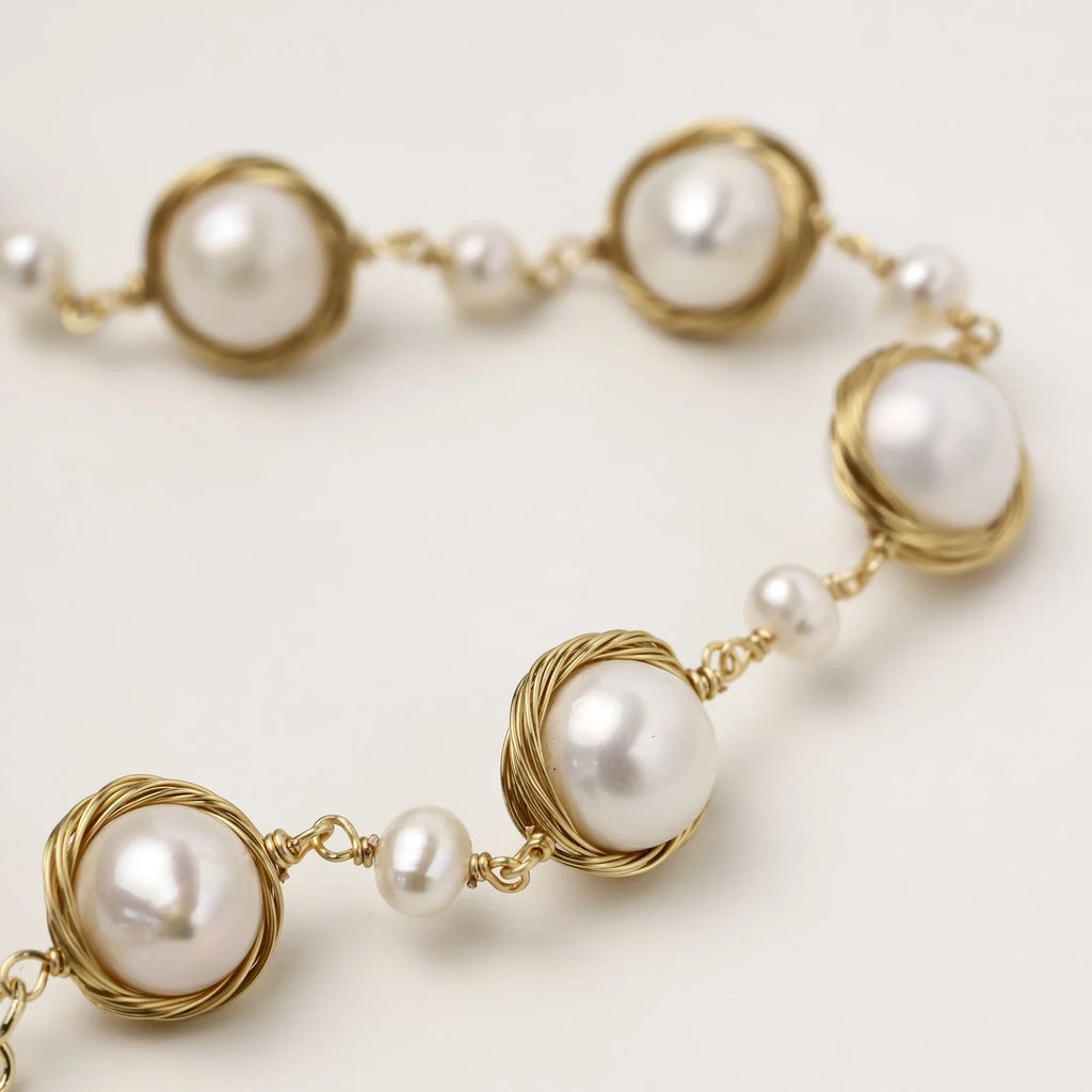 Gold wire-wrapped freshwater pearl bracelet with alternating pearl sizes on cream background, adjustable length