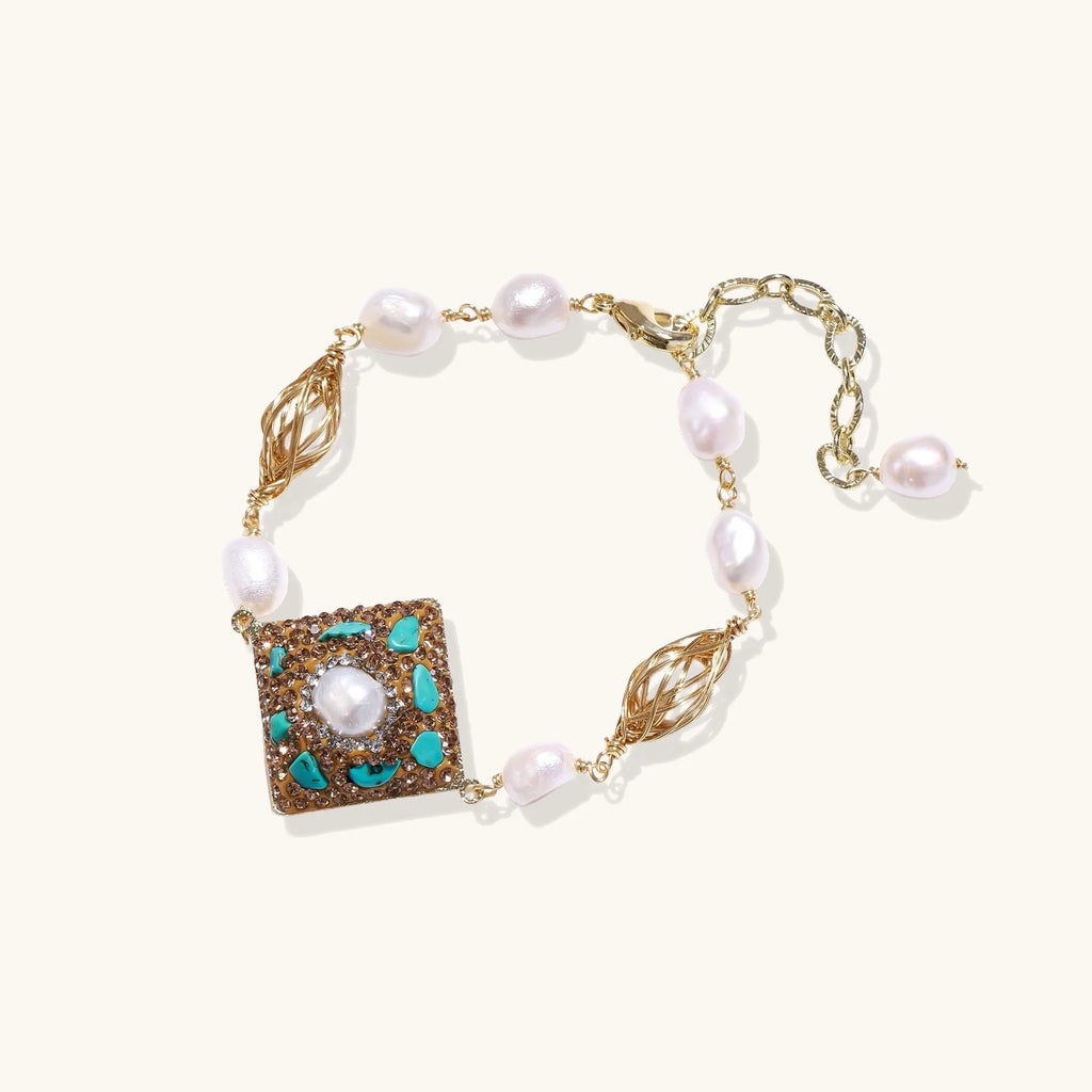 Gold-plated bracelet with baroque centerpiece, turquoise stones, freshwater pearls, and ornate chain links on cream background.