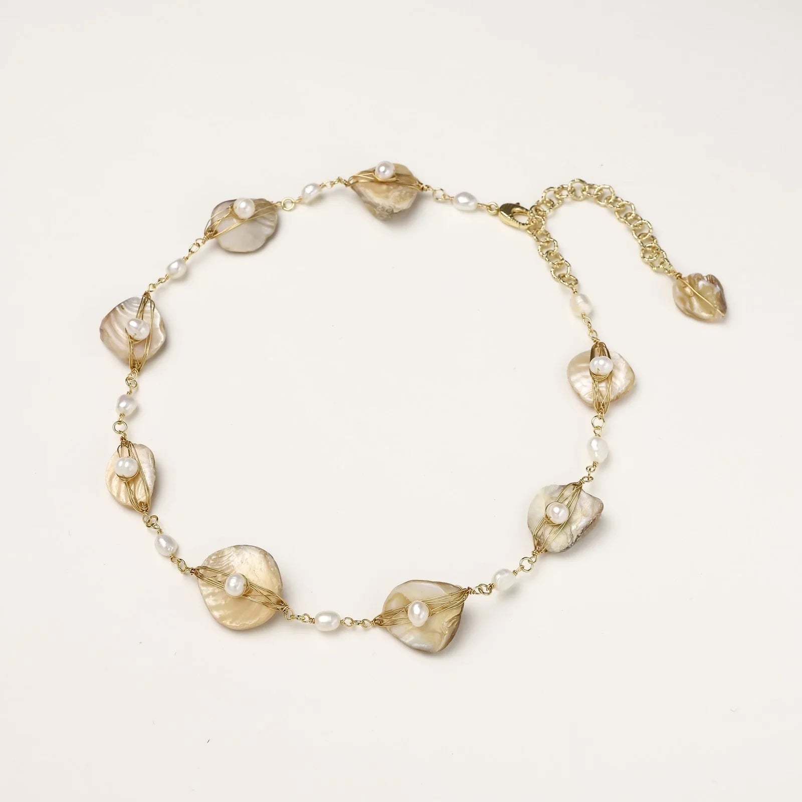 Gold-plated necklace with wire-wrapped shell pieces and freshwater pearls on neutral background, adjustable chain visible.