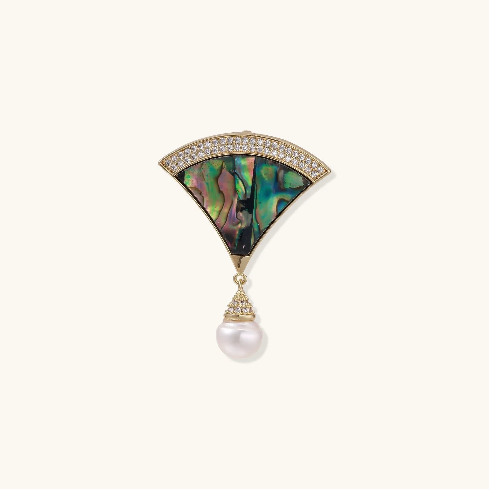 Gold fan-shaped brooch with iridescent abalone shell center, crystal border, and dangling white pearl on cream background