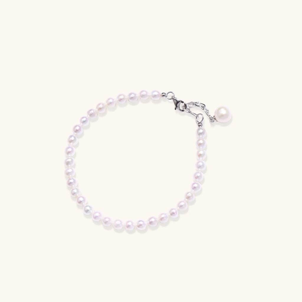 Delicate freshwater pearl bracelet with rhodium-plated silver clasp and single pearl drop charm on cream background