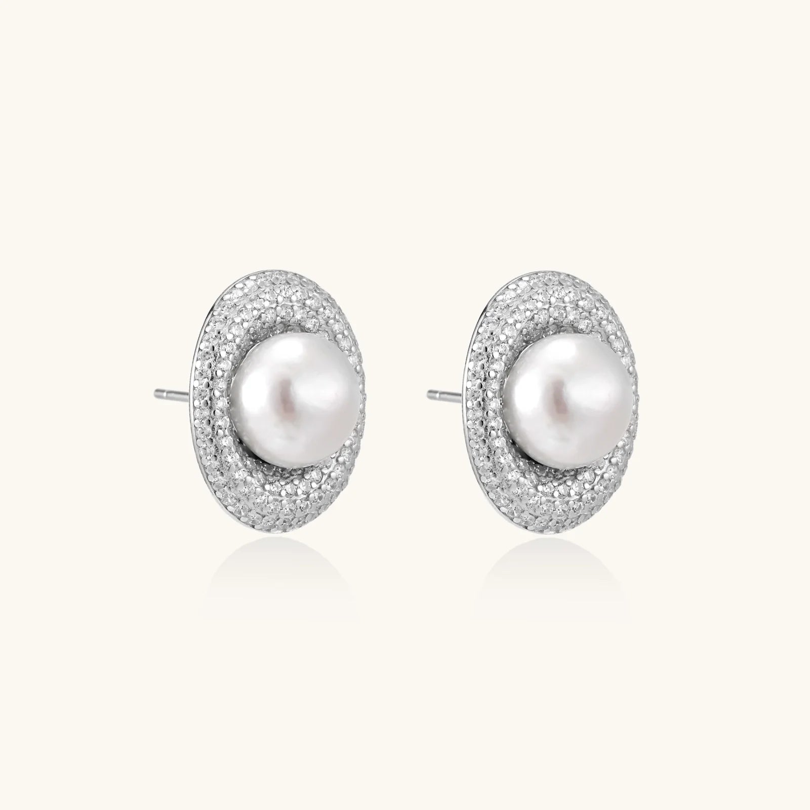 Oval rhodium-plated silver studs featuring freshwater pearls surrounded by pavé crystal halo on white background