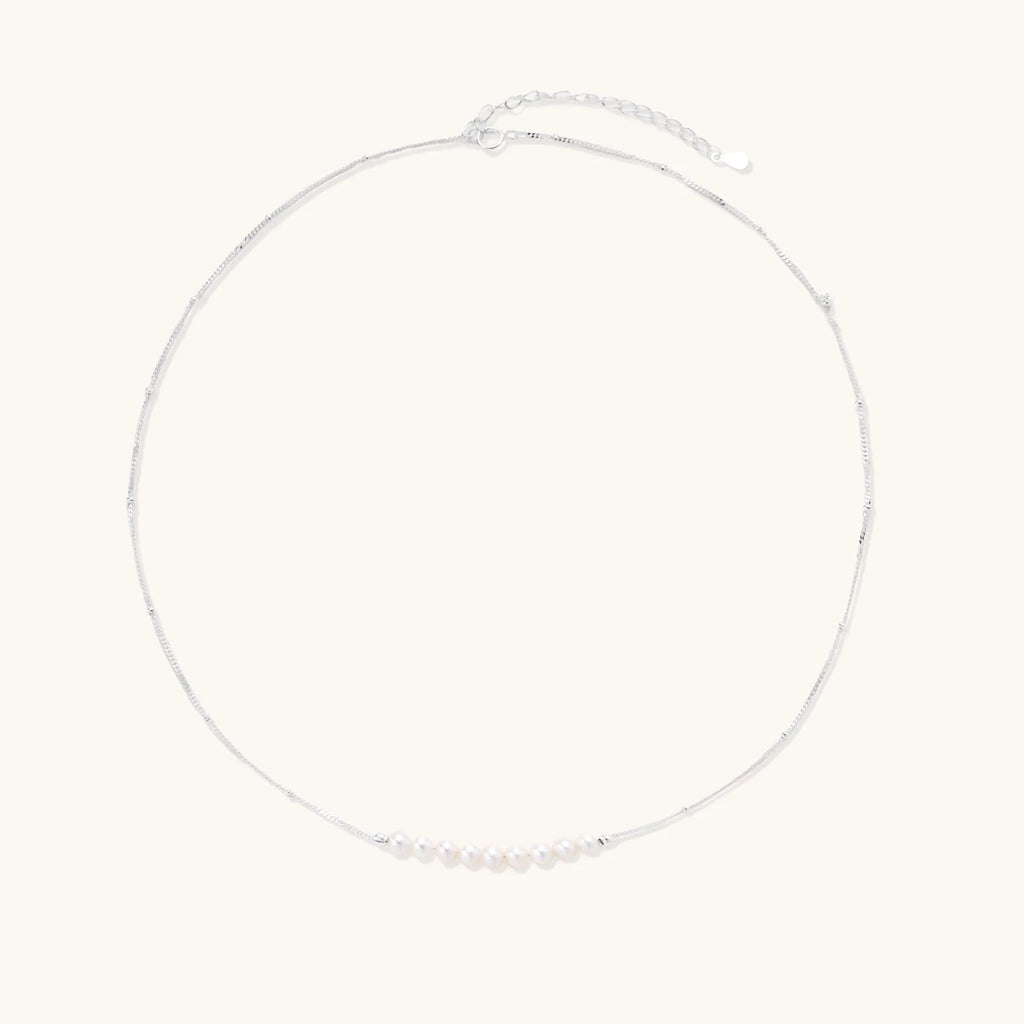 Delicate sterling silver chain necklace with small freshwater pearls arranged in a curved smile arc on cream background.