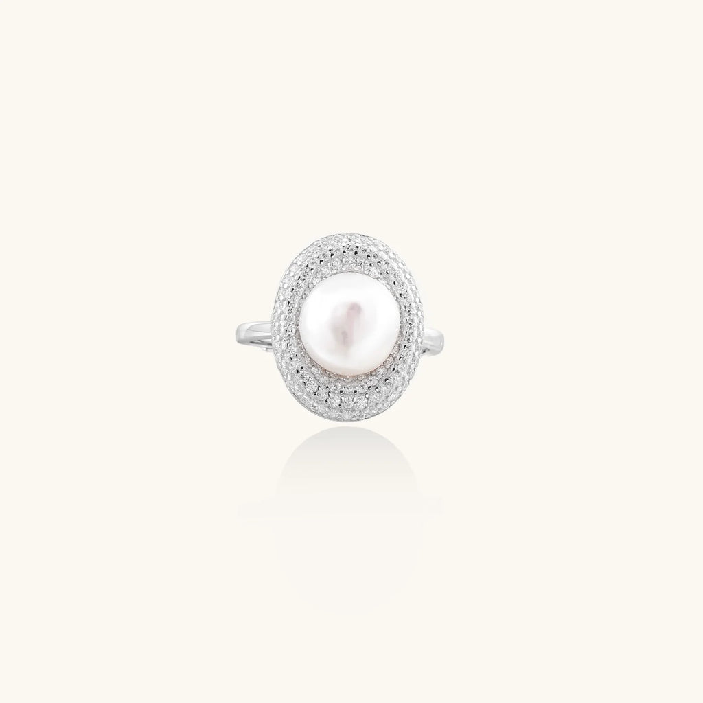 Silver ring with lustrous white pearl center surrounded by sparkling crystal halo on light background.