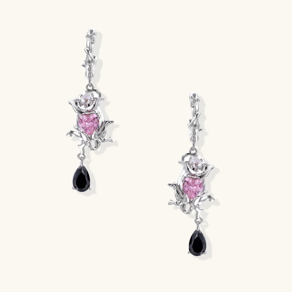 Silver-toned drop earrings with ornate rose design, pink zirconia center, and black teardrop stones on cream background