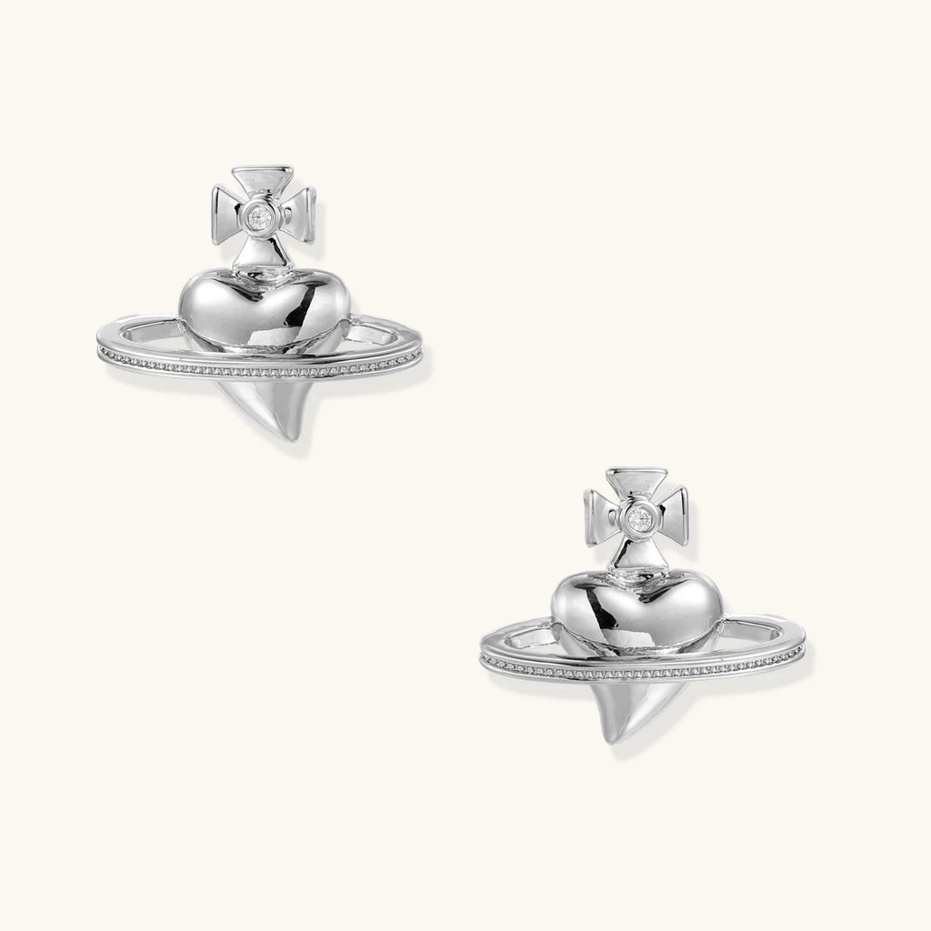 Polished white gold-plated Saturn planet stud earrings with orbital rings and crystal-centered cross on beige background