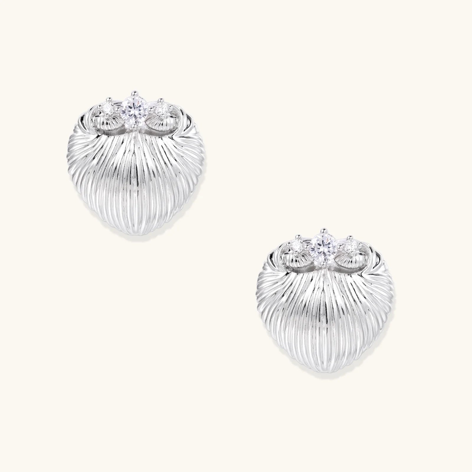 White gold-plated shell-textured stud earrings with three zirconia crystals on ridged surface against cream background.