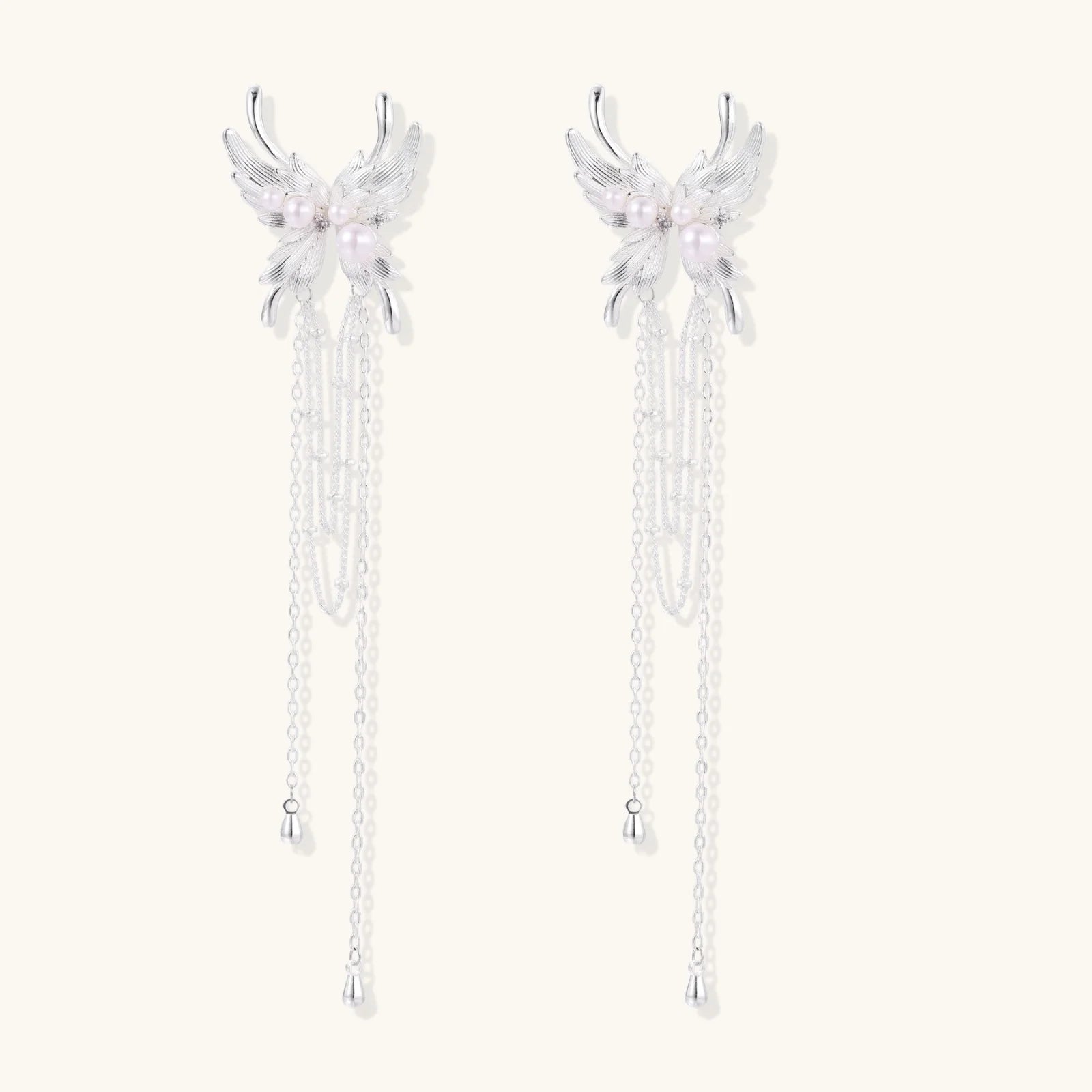 Elegant chandelier earrings with phoenix wing design, white pearls, and cascading silver chains on cream background