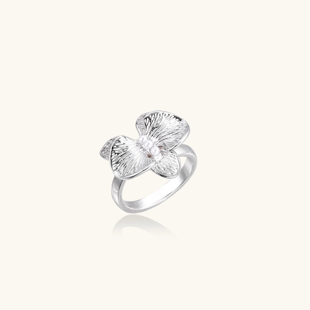 Silver-toned orchid ring with textured petals, pearl center accents, and sparkling zirconia stones on white background.