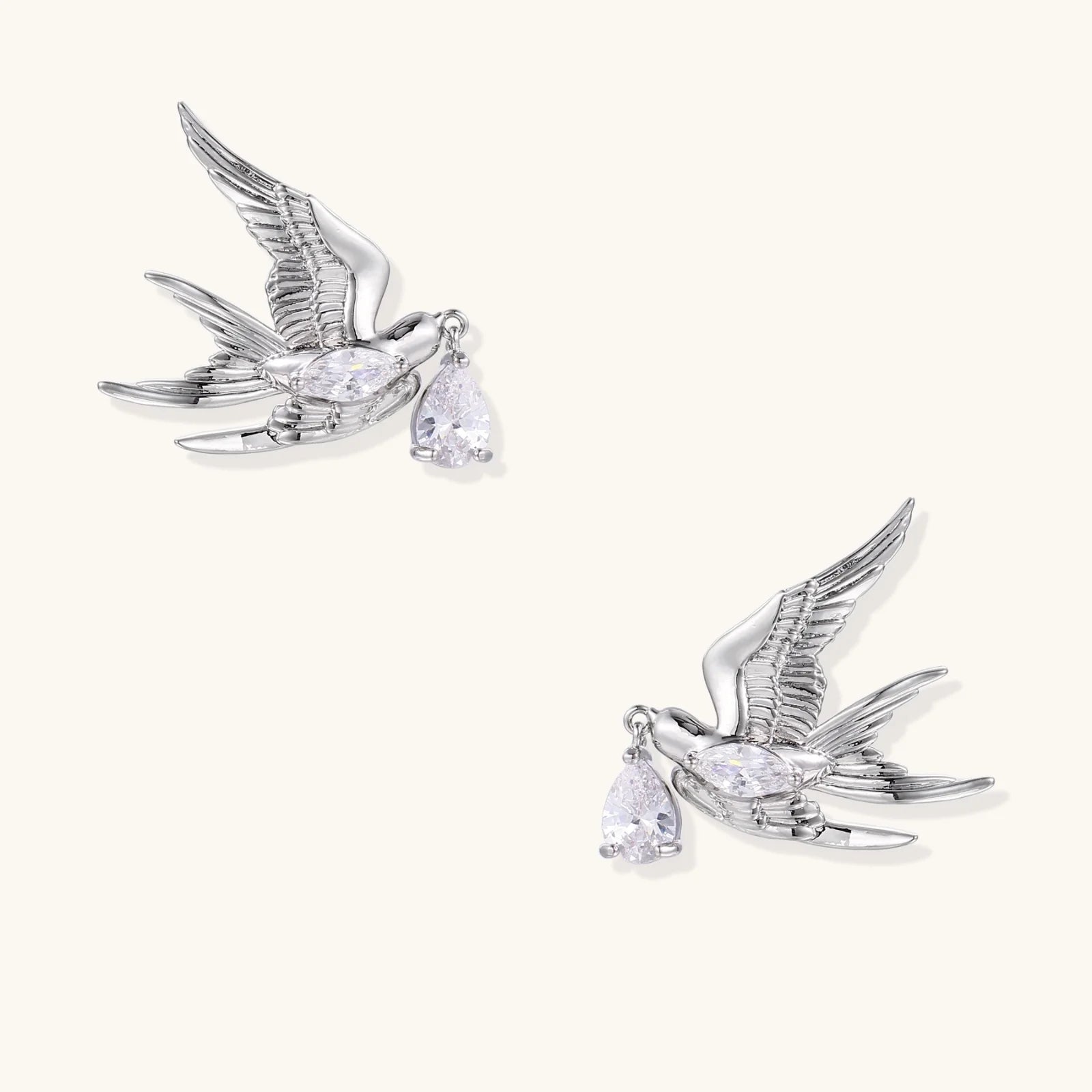 Silver-toned swallow stud earrings with detailed wings carrying teardrop zirconia crystals on white background