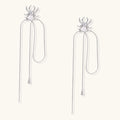 White gold plated spider earrings with pearl body and long threader chains on beige background