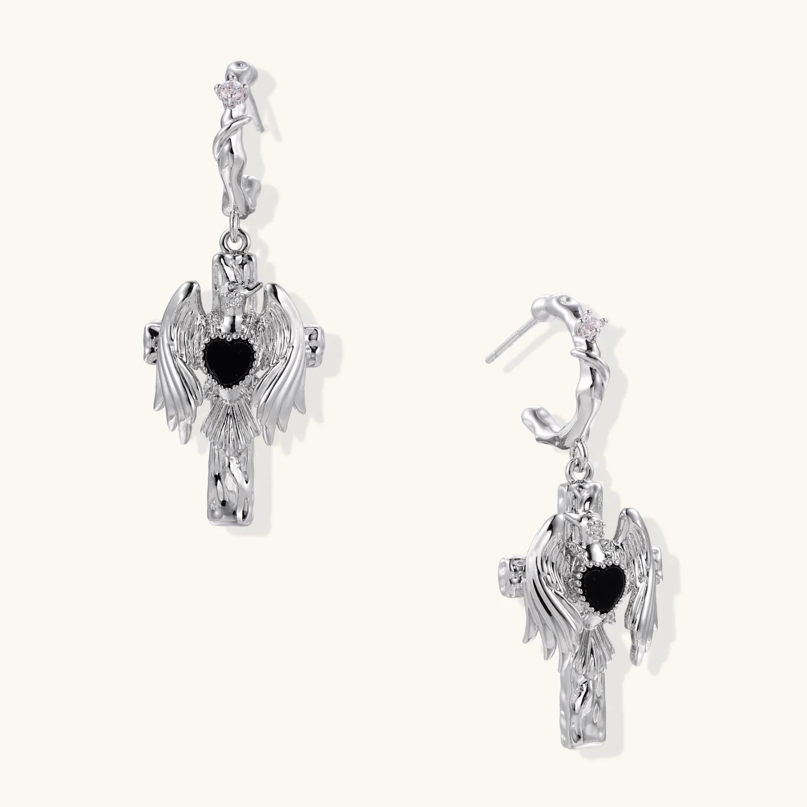 Silver drop earrings with twisted hoops and angel wings embracing black heart locket on white background.