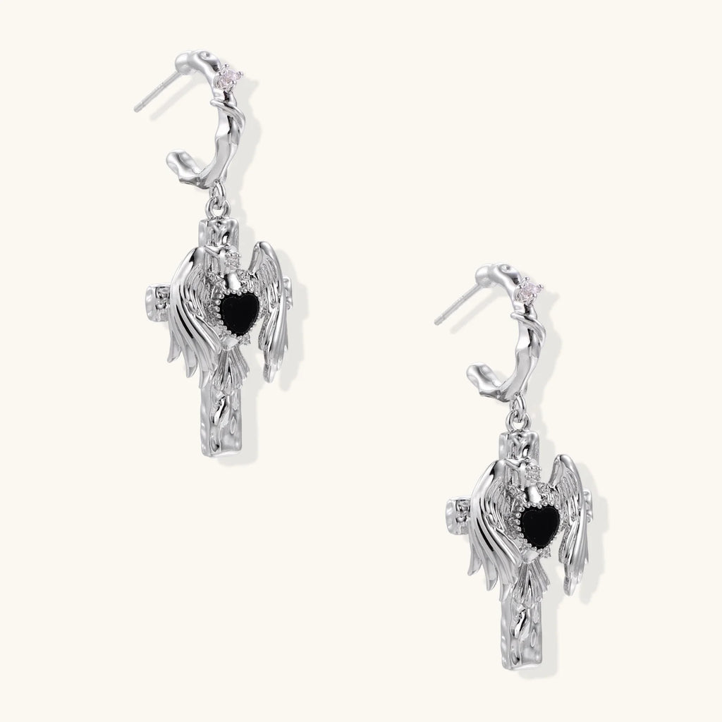 Silver drop earrings with twisted hoops and angel wings embracing black heart locket on white background.
