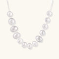 Graduated pearl-finish silver discs forming an organic bubble bib necklace on delicate chain against cream background.