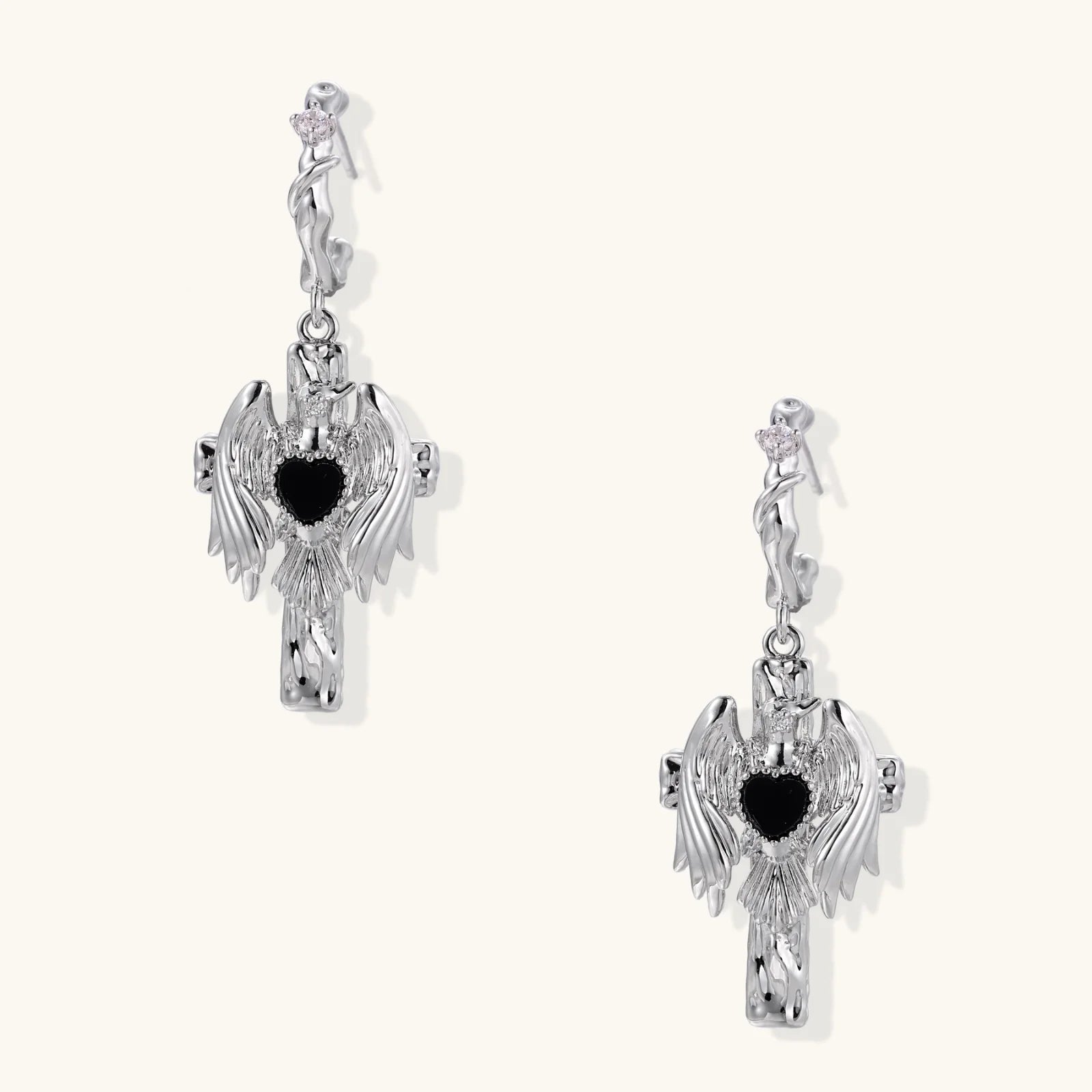 Silver drop earrings with twisted hoops and angel wings embracing black heart locket on white background.