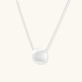 Minimalist brushed sterling silver dome pendant on delicate chain against cream background, showing matte textured finish