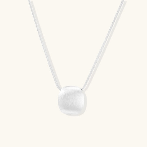 Minimalist brushed sterling silver dome pendant on delicate chain against cream background, showing matte textured finish