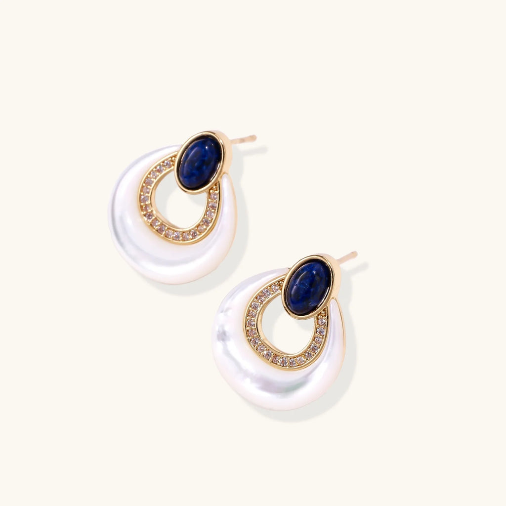 Gold drop earrings with oval lapis lazuli, crystal-paved frame, and iridescent mother-of-pearl teardrop on cream background
