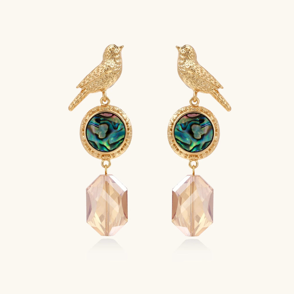 Gold-plated bird stud earrings with iridescent abalone shell medallions and champagne crystal drops on cream background