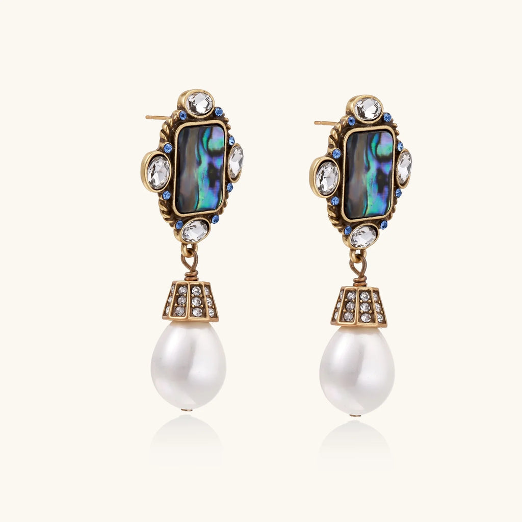 Ornate gold-plated earrings with iridescent abalone shell, crystals, blue stones, and white pearl drops on cream background.