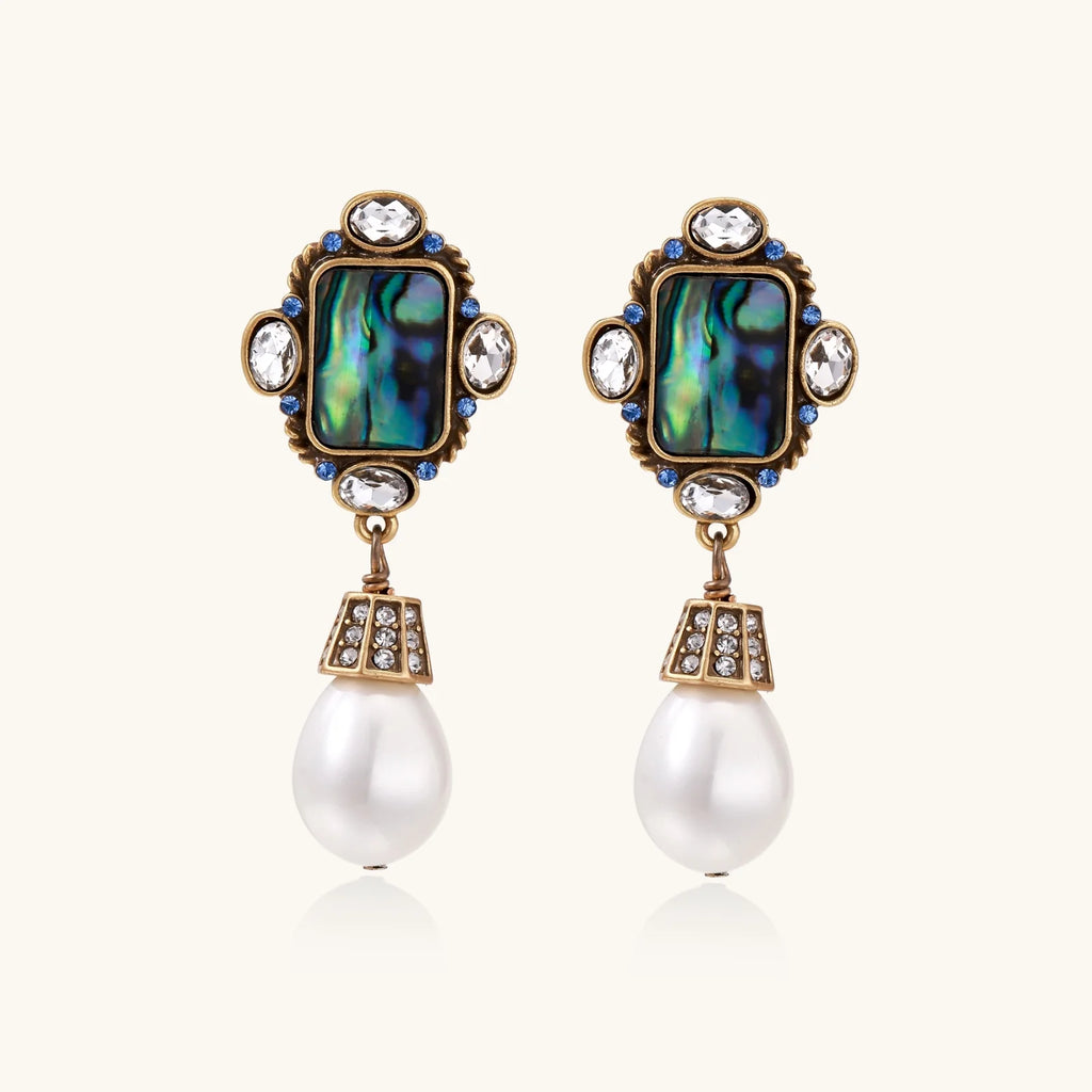 Ornate gold-plated earrings with iridescent abalone shell, crystals, blue stones, and white pearl drops on cream background.