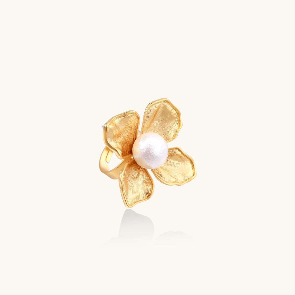 Gold-plated flower ring with textured petals and white cotton pearl center on cream background