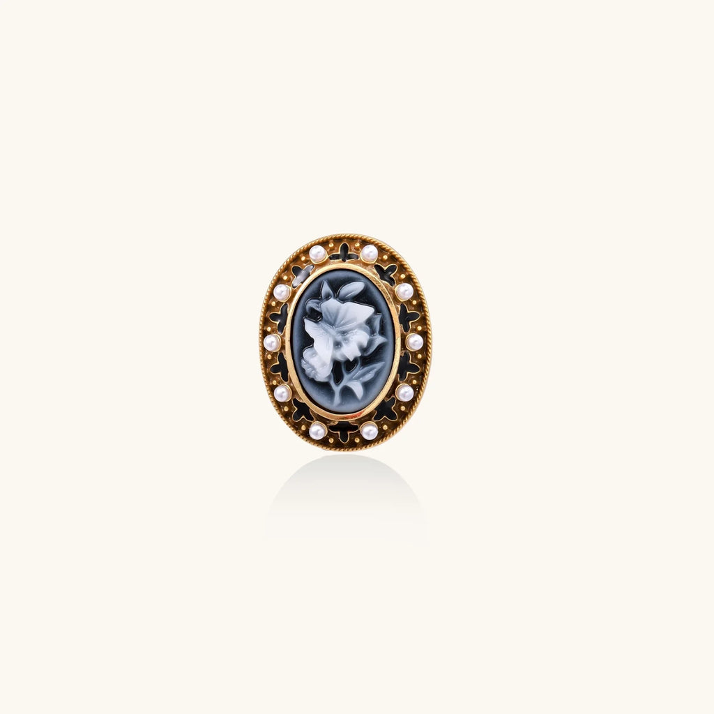 Gold-plated ring with oval blue floral cameo, pearl accents, and black enamel detailing on white background.