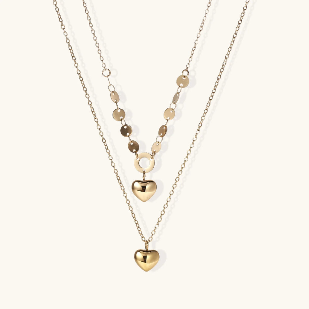 Three-layer 14K gold plated necklace with coin discs and dual heart pendants on cream background