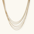 Seven delicate gold-plated snake chains create an elegant layered necklace on a neutral background.