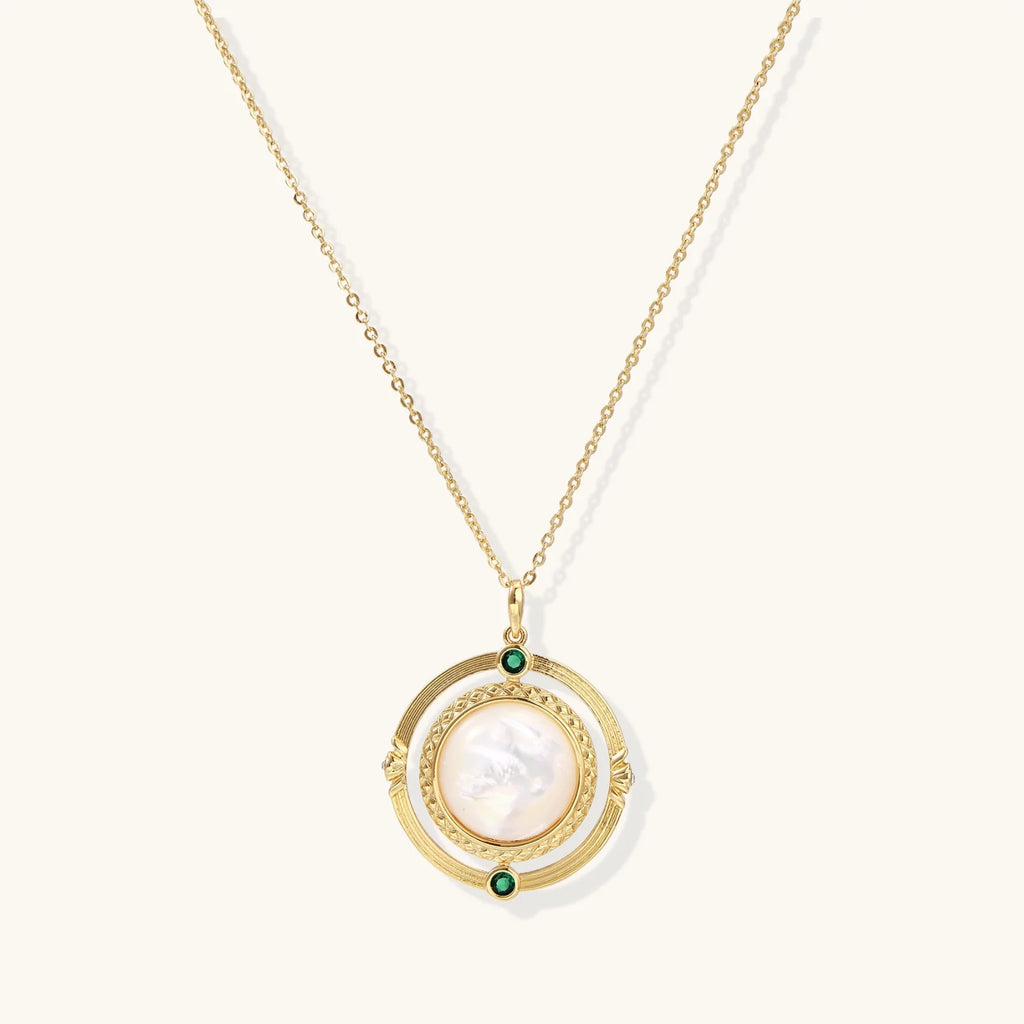 Gold pendant necklace with circular orbital design, iridescent mother-of-pearl center, and green zirconia accents
