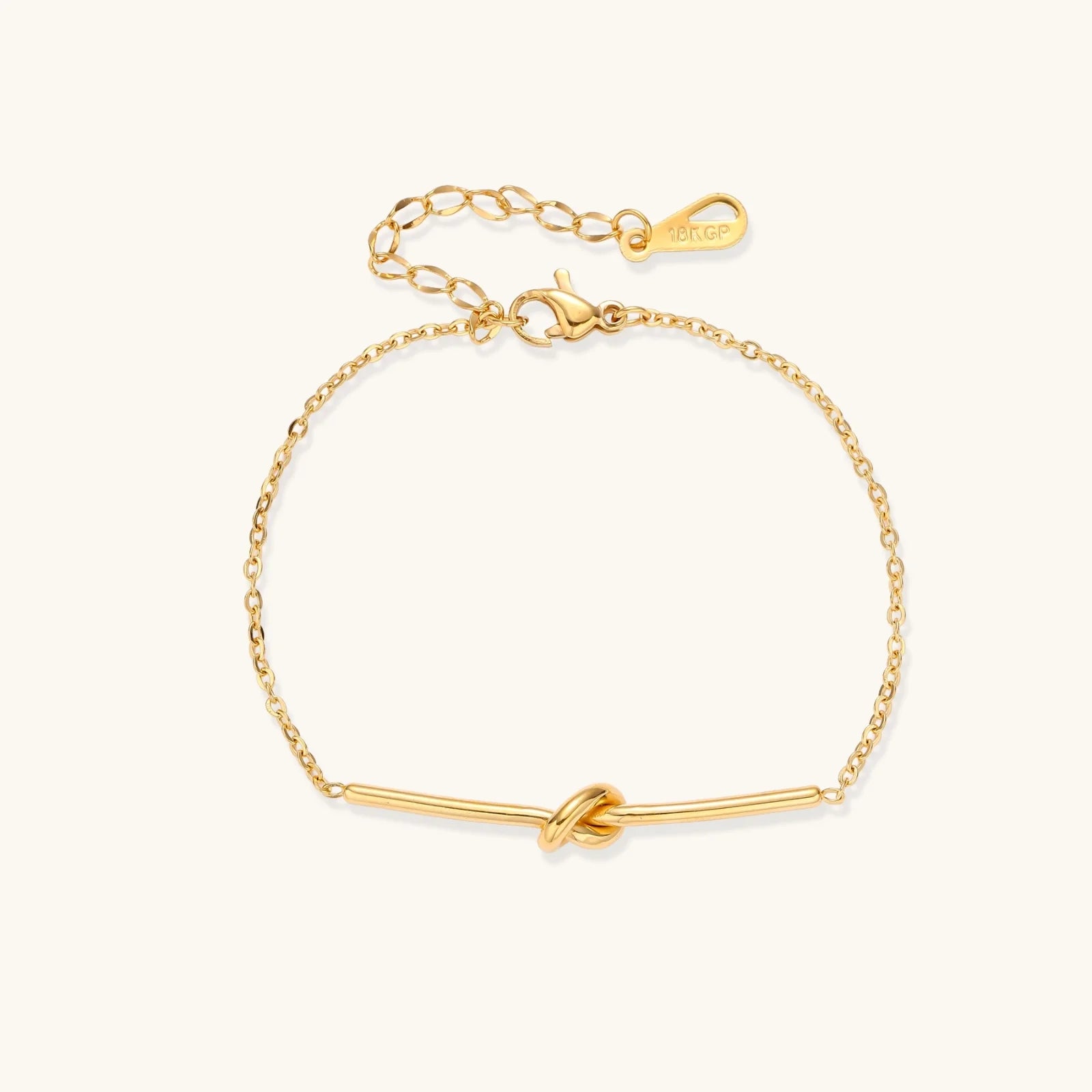 Delicate gold chain bracelet with minimalist bar and centered knot detail on cream background