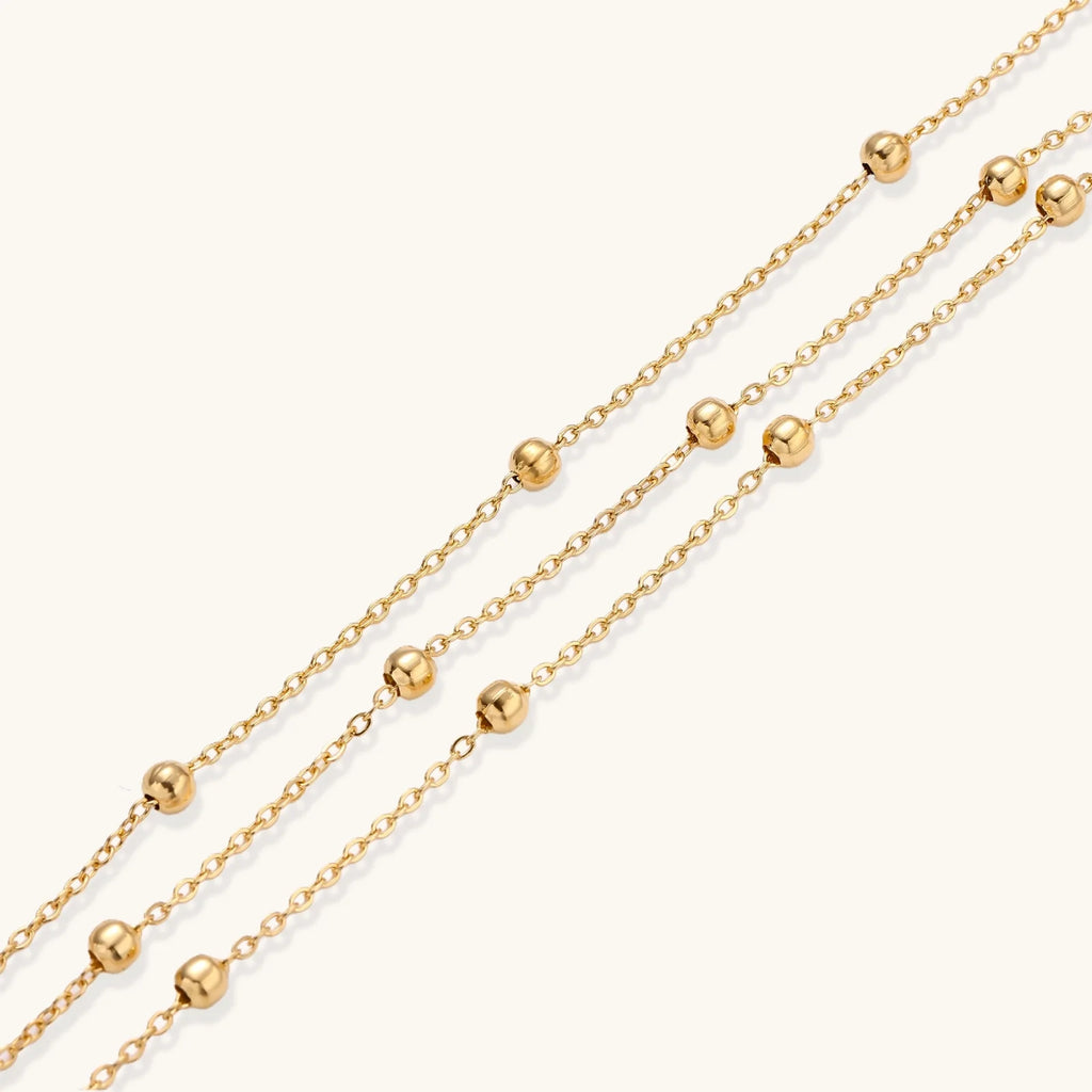 Three-strand gold-plated bracelet with clustered ball beads and adjustable clasp on cream background