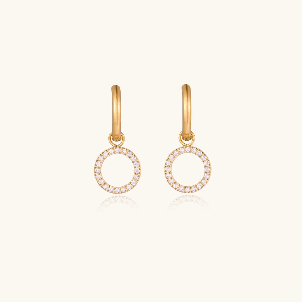 Gold-plated huggie hoop earrings with CZ-studded open circle charms on beige background
