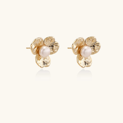 Gold-plated flower stud earrings with textured petals and centered freshwater pearl on beige background