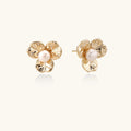 Gold-plated flower stud earrings with textured petals and centered freshwater pearl on beige background