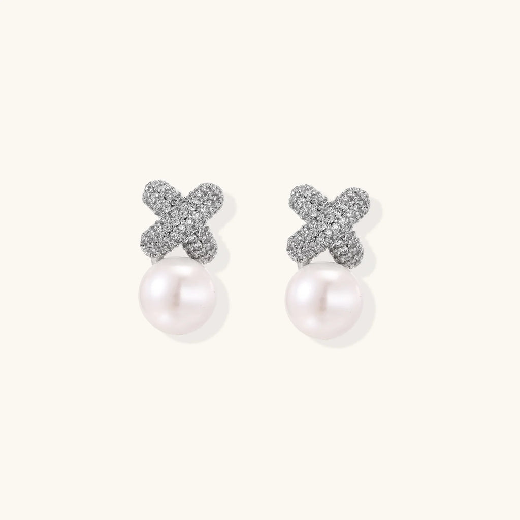 White gold plated studs featuring pavé X-shaped tops with freshwater pearl drops on cream background.