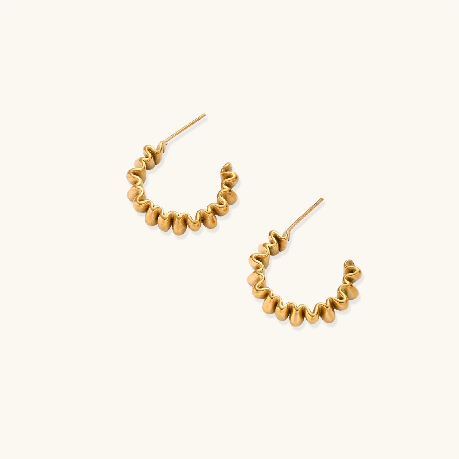 Sculptural gold-plated hoop earrings with continuous twisted spiral design on cream background