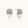 Curved pavé diamond studs in white gold-plated brass cradle lustrous freshwater pearls against cream background