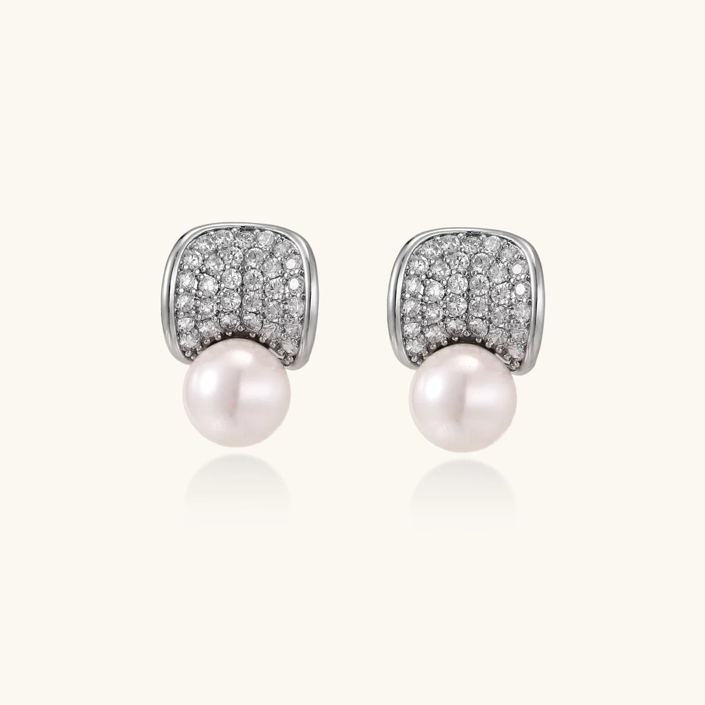 Curved pavé diamond studs in white gold-plated brass cradle lustrous freshwater pearls against cream background
