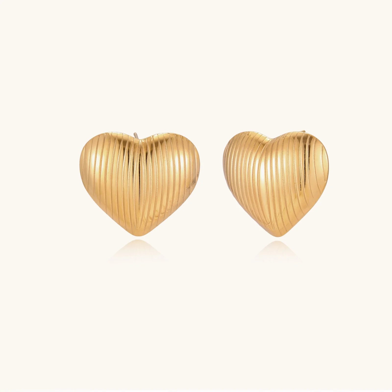 Gold heart-shaped stud earrings with parallel ridged texture on cream background