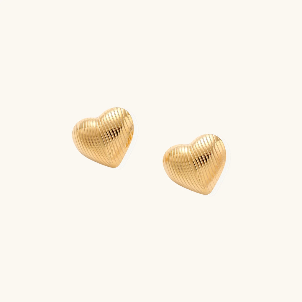 Gold heart-shaped stud earrings with parallel ridged texture on cream background