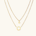 Gold layered necklace set with sunburst and smiley face pendants on delicate chains against white background.