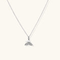 Delicate white gold plated whale tail pendant with pavé crystals on silver chain against cream background.