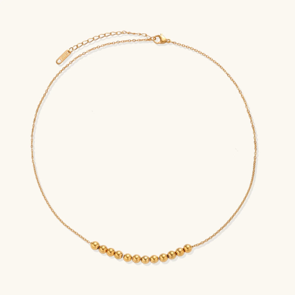 Delicate gold-plated necklace with graduated spherical beads forming gentle smile curve on beige background