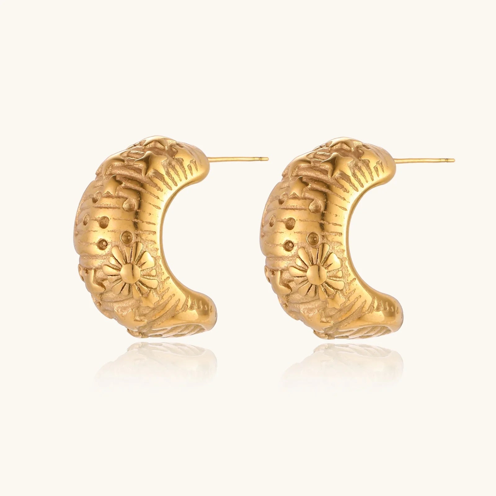 Gold-plated chunky hoop earrings with sun and star engravings on white background, showing detailed celestial pattern work.