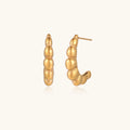 Gold-plated sculptural hoop earrings with chunky segmented design on cream background