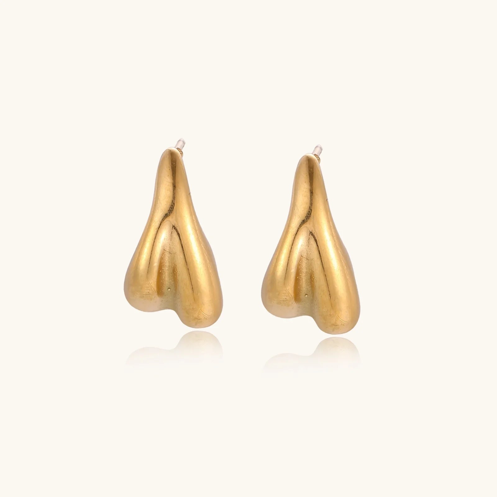 Pair of sculptural gold stud earrings with twisted organic forms on cream background
