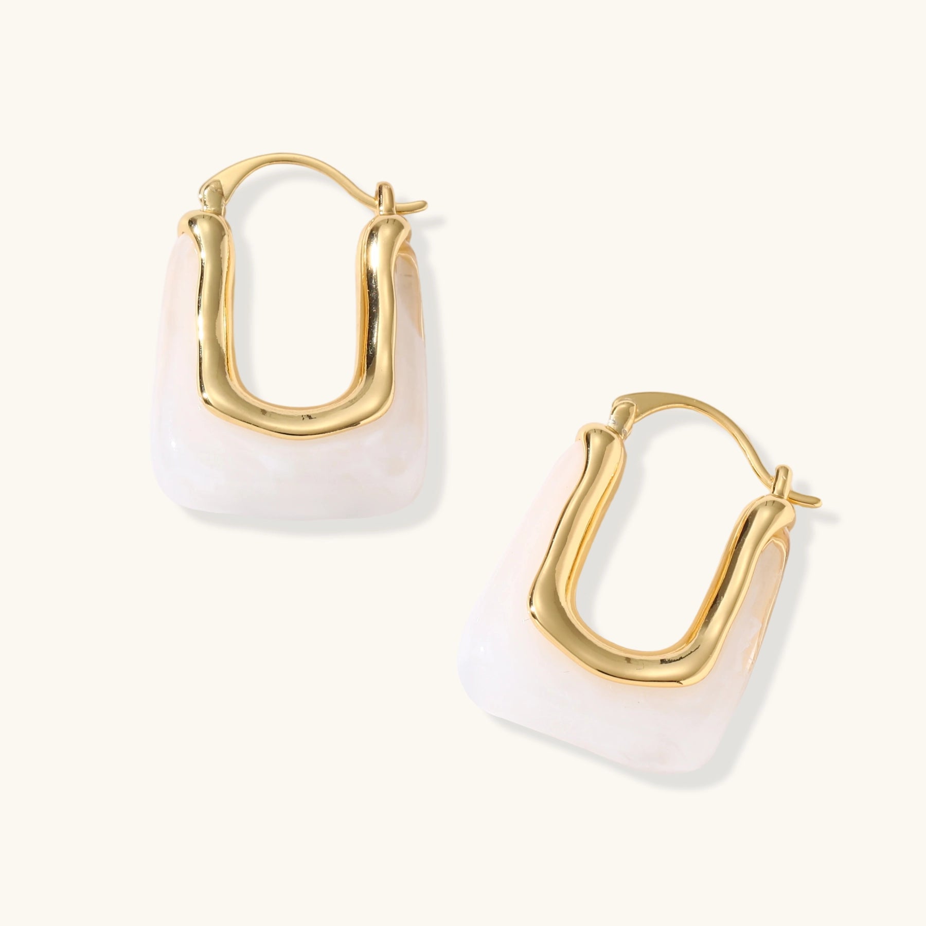 Sculptural gold-plated hoop earrings with flowing curved design and lever-back closure on cream background.