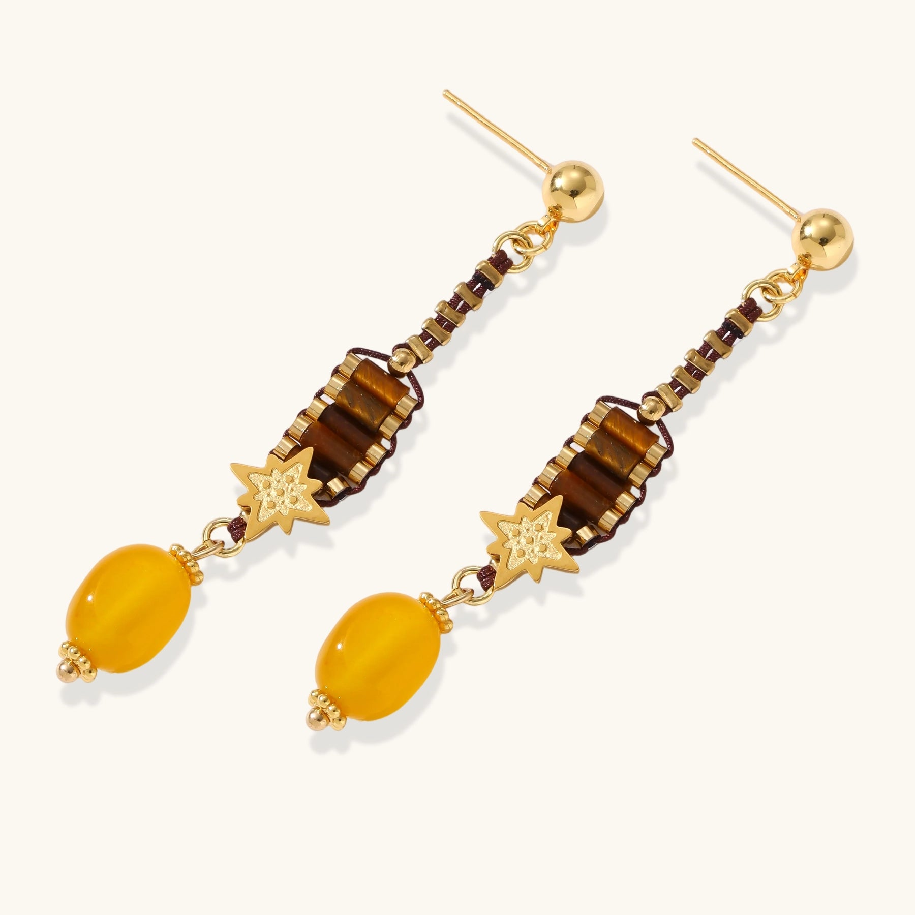 Gold-plated dangle earrings with brown gemstones, star charms, and yellow amber drops on cream background.